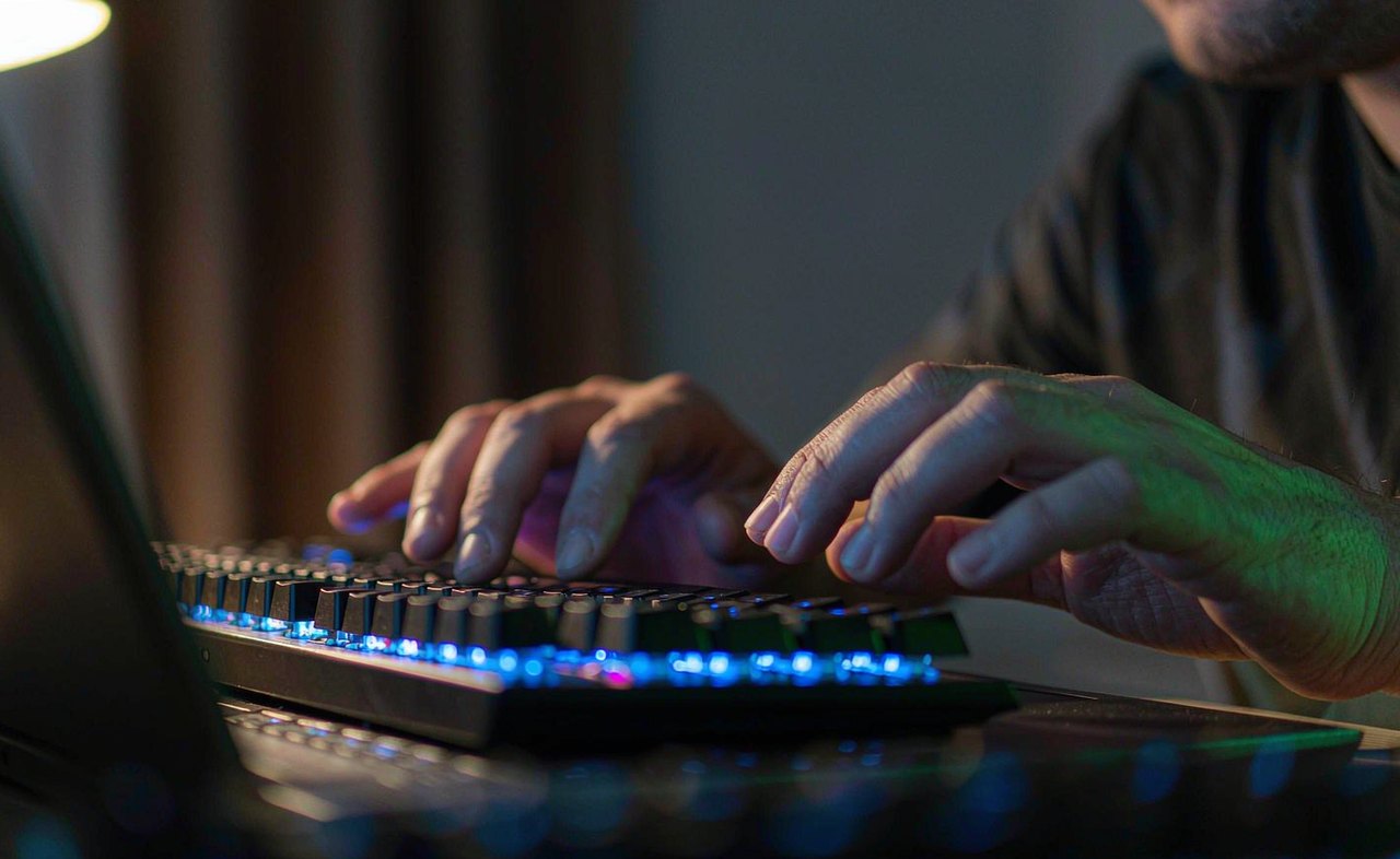 Close-up of hands typing on a backlit laptop keyboard in low light, with one hand paused over the keys