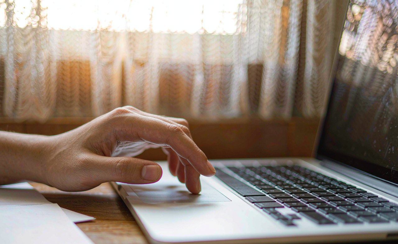 A close-up of a hand hovering above an unresponsive silver laptop touchpad on a wooden desk, warm afternoon light, shallow depth of field